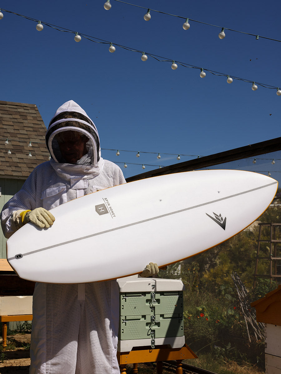 Beekeeper holding the Firewire Spun Honey surfboard, showcasing its honeycomb-inspired design