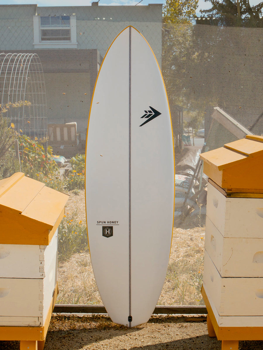 Firewire Spun Honey surfboard standing between beehives, deck view