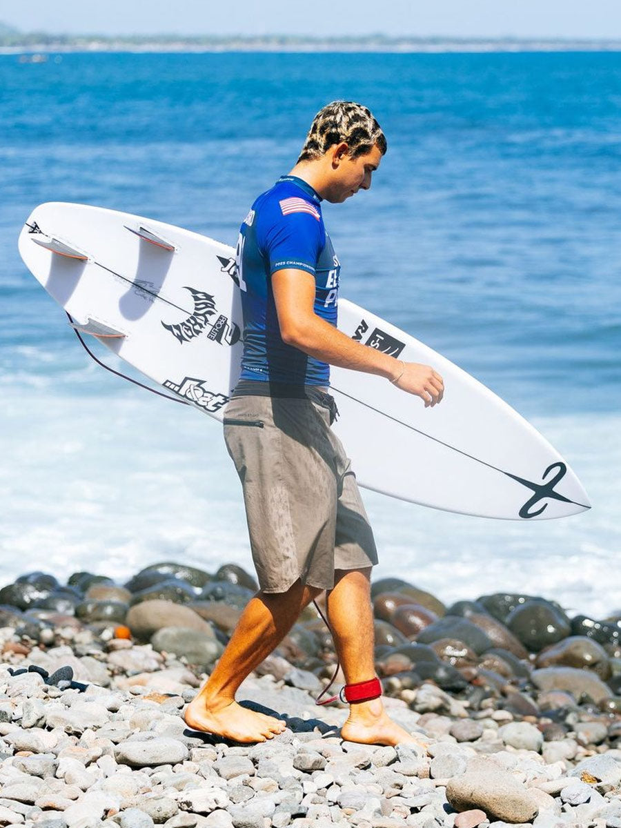 Surfer carrying the Lost Formula 1 Squash surfboard to the water