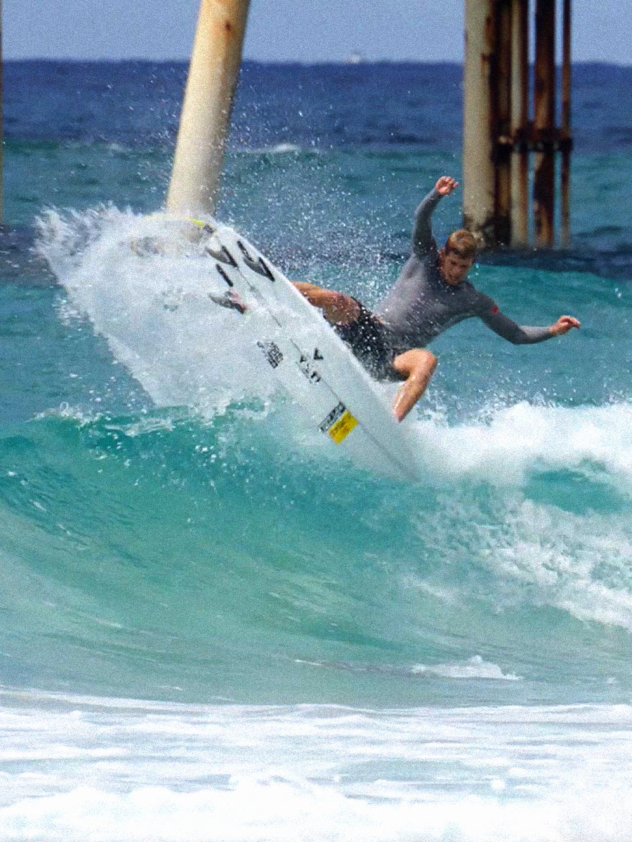 Surfer carving a wave near a pier on the Pyzel White Tiger surfboard